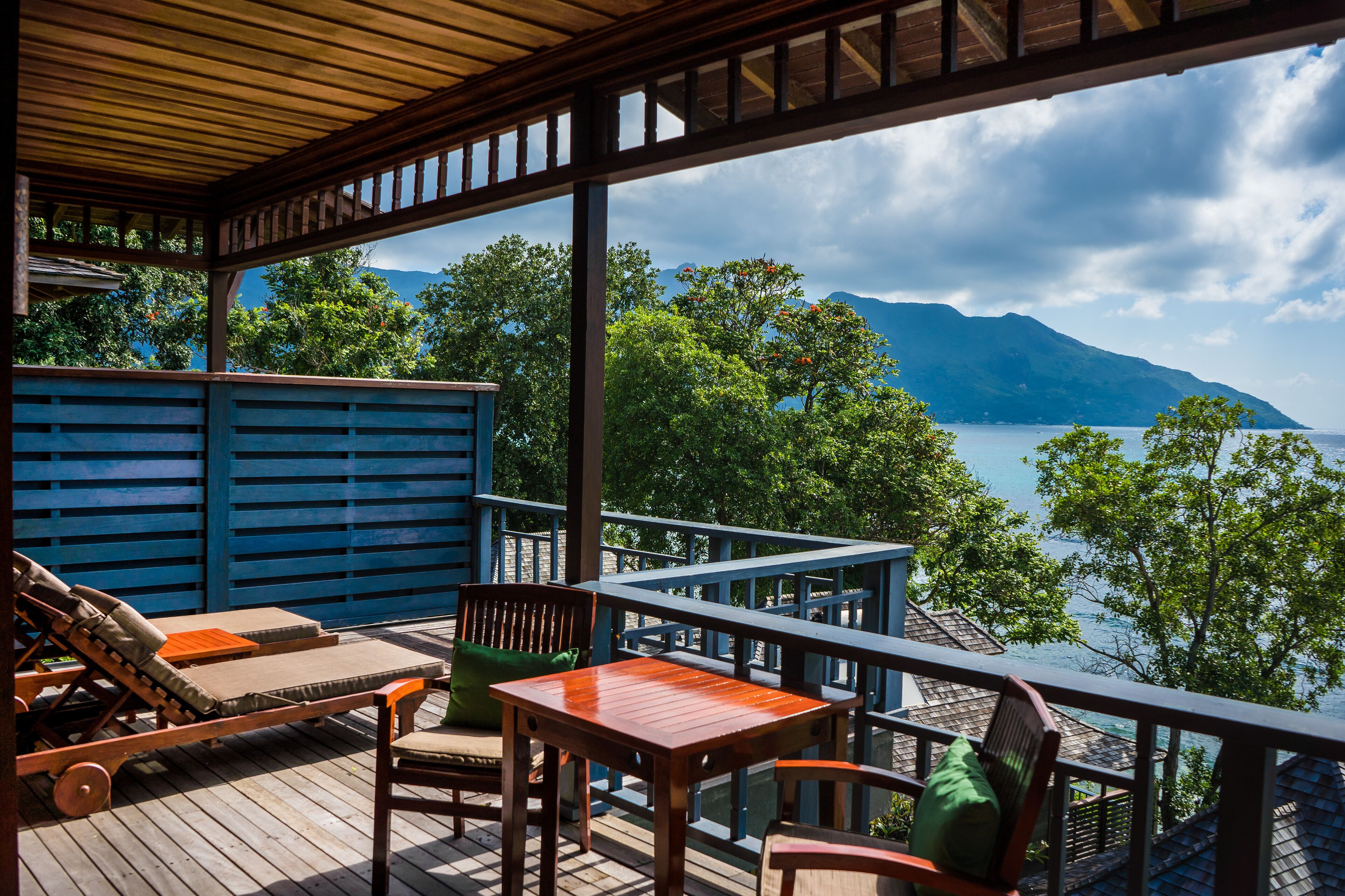 Eine Holzterrasse mit Gartenmöbeln, Blick auf einen See und Berge im Hintergrund.