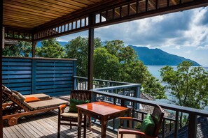 Eine Holzterrasse mit Gartenmöbeln, Blick auf einen See und Berge im Hintergrund.