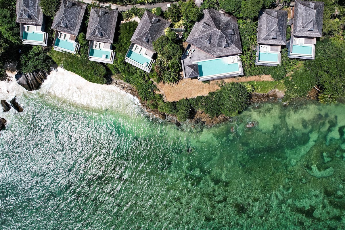 Eine Luftaufnahme eines Küsteneigentums mit mehreren Häusern, die jeweils einen Swimmingpool besitzen, umgeben von üppiger Vegetation und einem Strand.