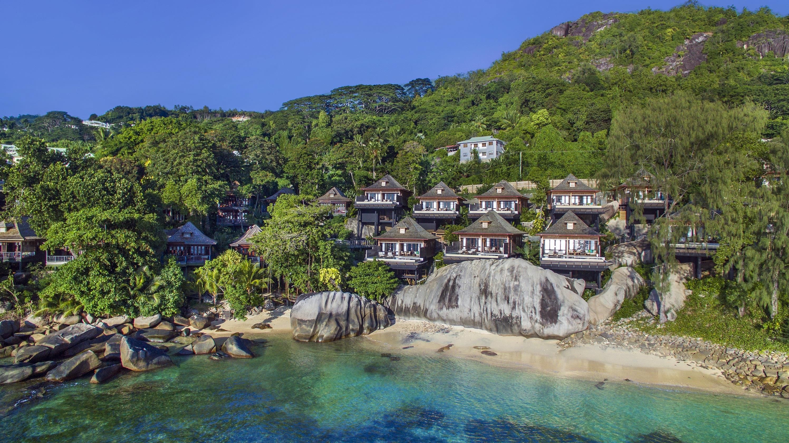 A coastal resort with multiple buildings, a clear beach, and lush greenery.