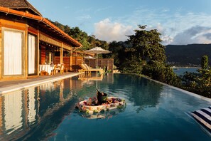 A pool with a floating bar area, lounge chairs, and a wooden building with a covered patio. - Hilton Seychelles Northolme Resort & Spa (Mahé Island)