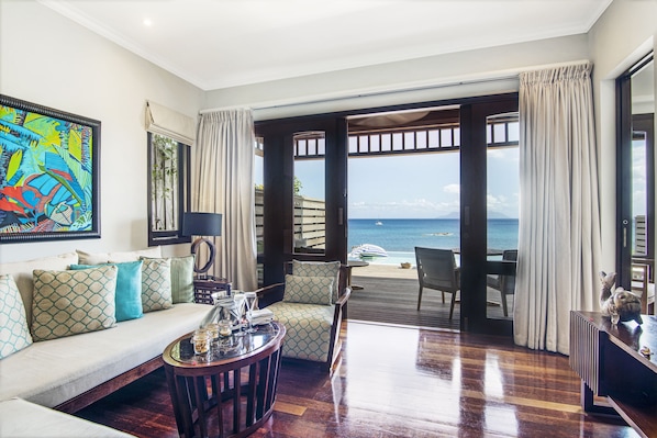 A spacious living room with a wooden floor, a sofa with patterned cushions, a coffee table, and a large painting on the wall. - Hilton Seychelles Northolme Resort & Spa (Mahé Island)