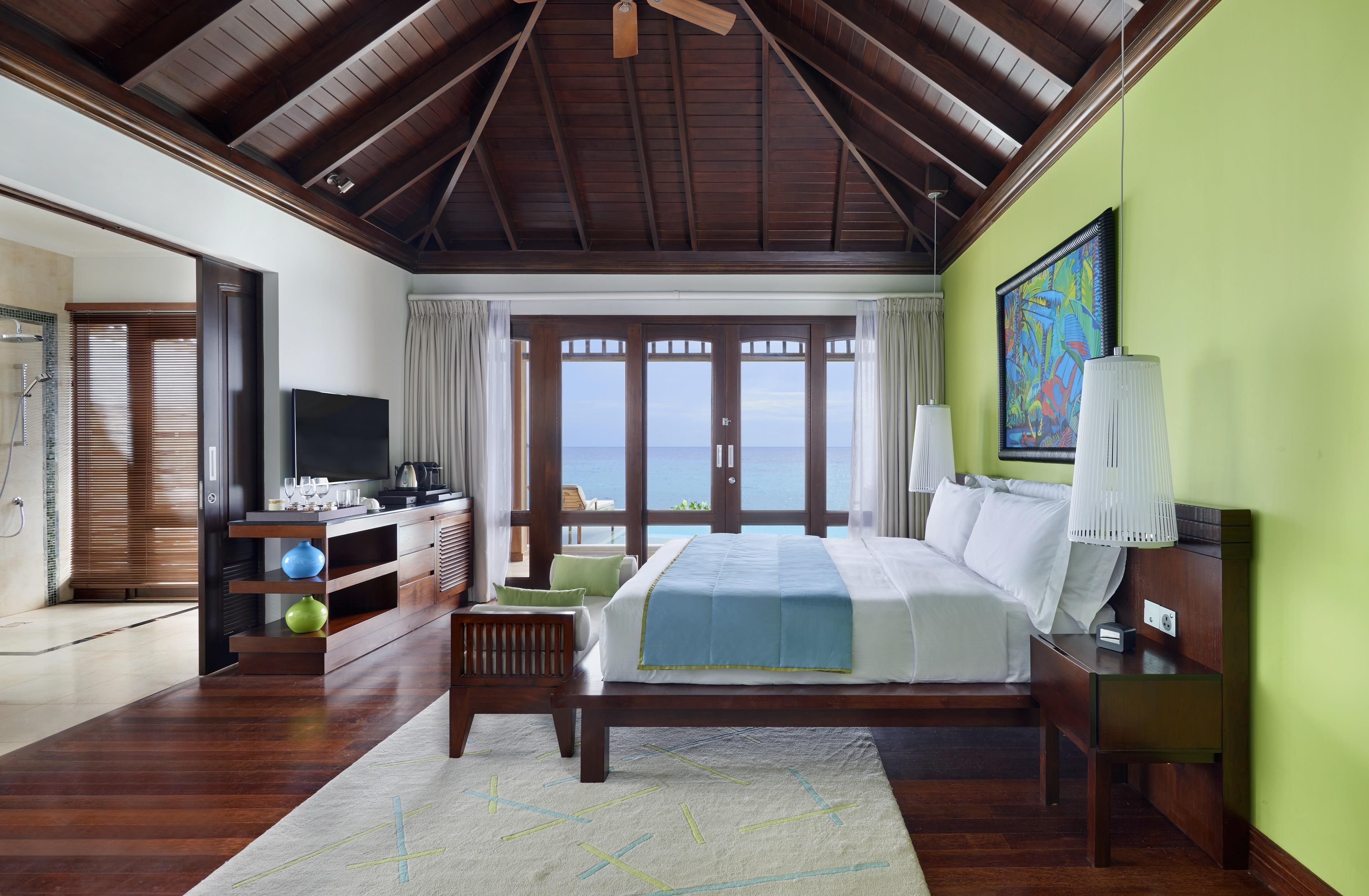 A spacious bedroom with a large bed, a television, and a view of the sea through the windows.