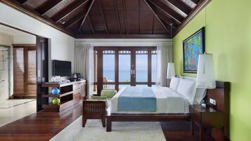 A spacious bedroom with a large bed, a television, and a view of the sea through the windows.