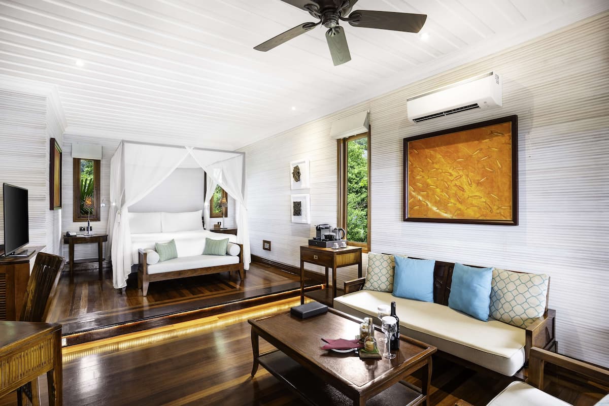 Ein geräumiges Zimmer mit Holzboden, Deckenventilator, großem Gemälde, Sofa, Couchtisch und Fernseher.