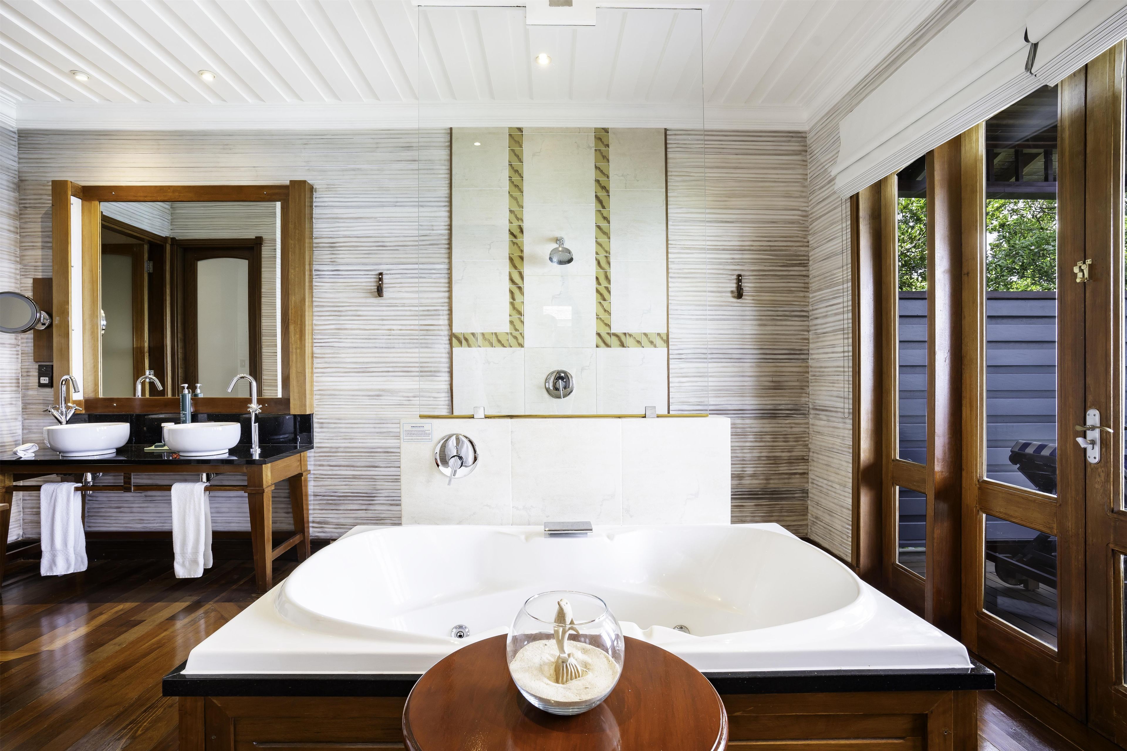 A modern bathroom with a large bathtub, dual sinks, and a large mirror.