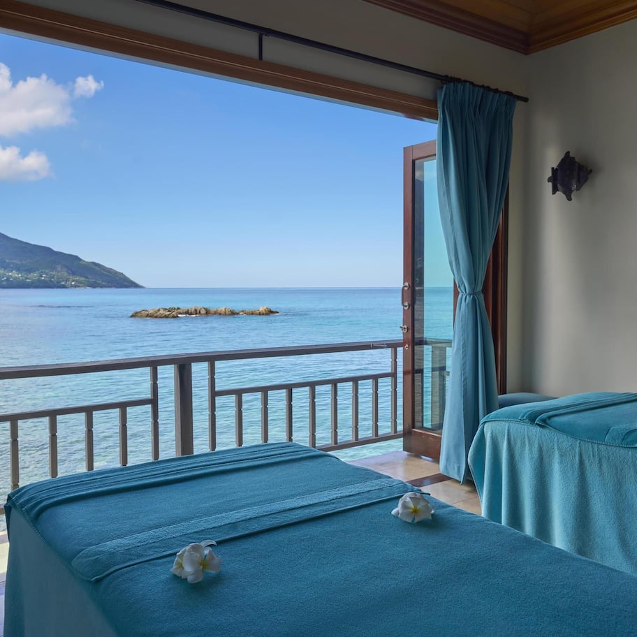 A room with two beds, a view of the sea, and a balcony with a railing.