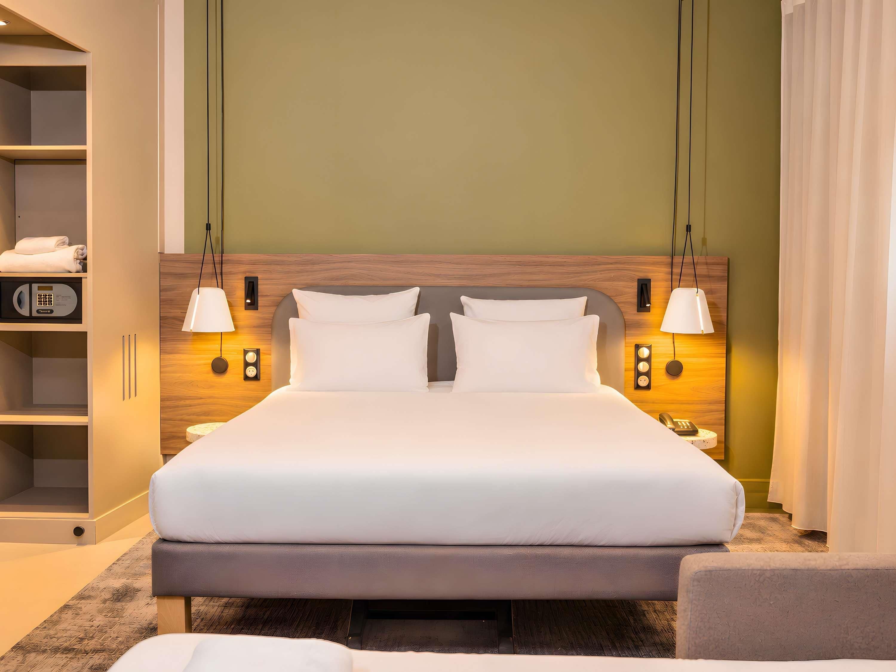 Habitación de hotel con una cama grande, lámparas de noche, un armario y un panel de control.