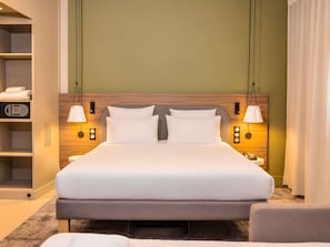 A hotel room with a large bed, bedside lamps, a wardrobe, and a control panel.