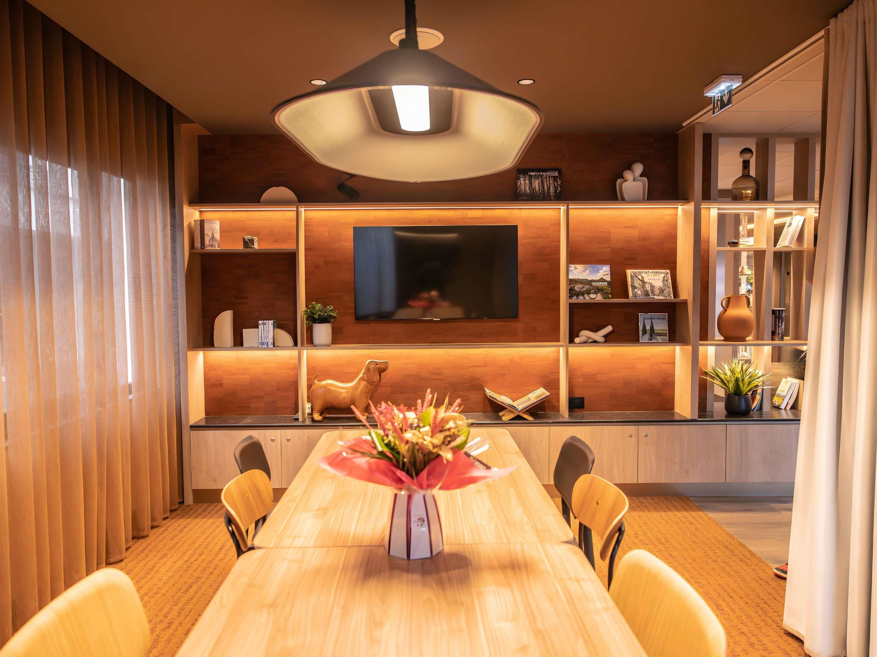 A modern dining area with a wooden table, chairs, a central vase, and a television mounted on the wall.