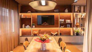 A modern dining area with a wooden table, chairs, a central vase, and a television mounted on the wall.