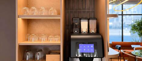 Une machine à café dotée d’un écran numérique, des verres élégants disposés sur des étagères et une vue sur la ville grâce à de grandes fenêtres.