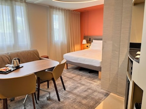 A hotel room with a bed, a desk with a tray of breakfast items, a sofa, and a carpeted floor.