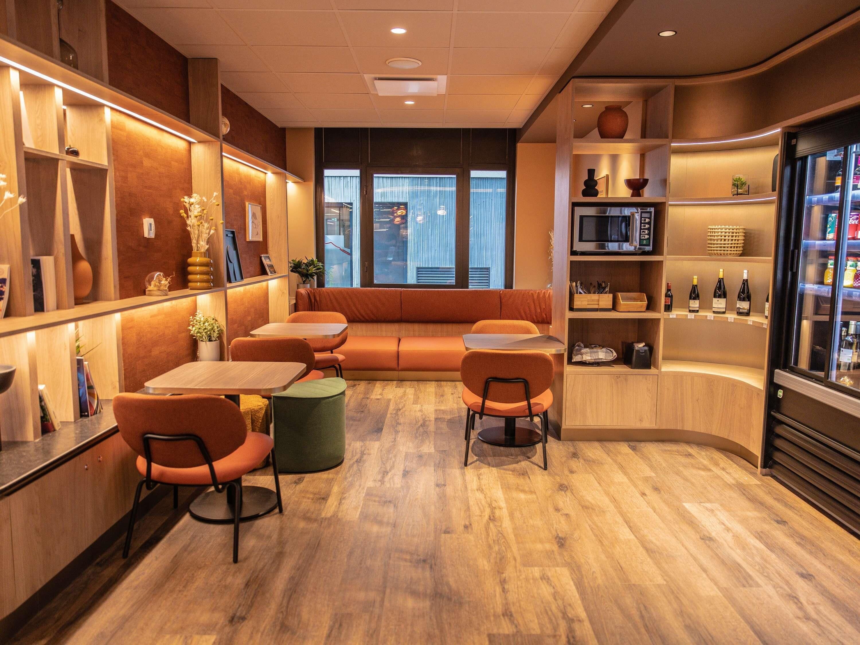 Een modern interieur met een zithoek, tafels en een koelkast vol drankjes.