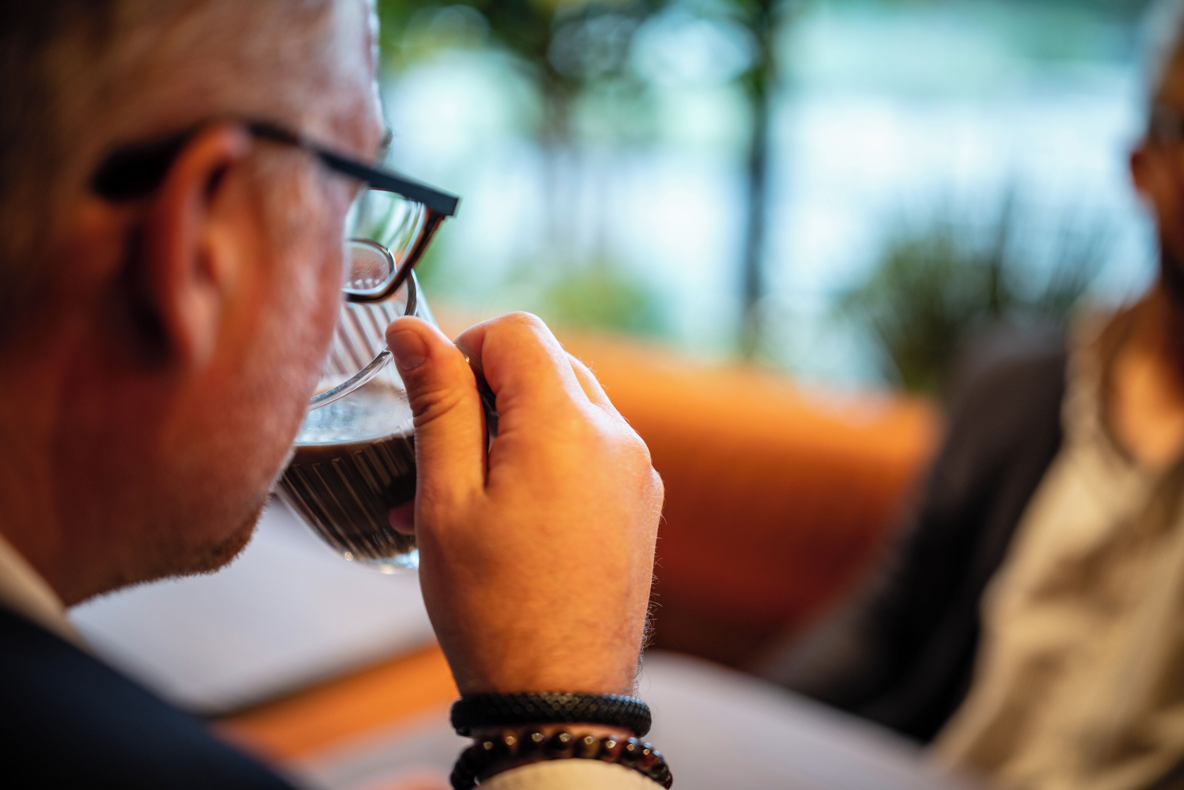 A person holding a glass, with a blurred background suggesting an indoor setting.