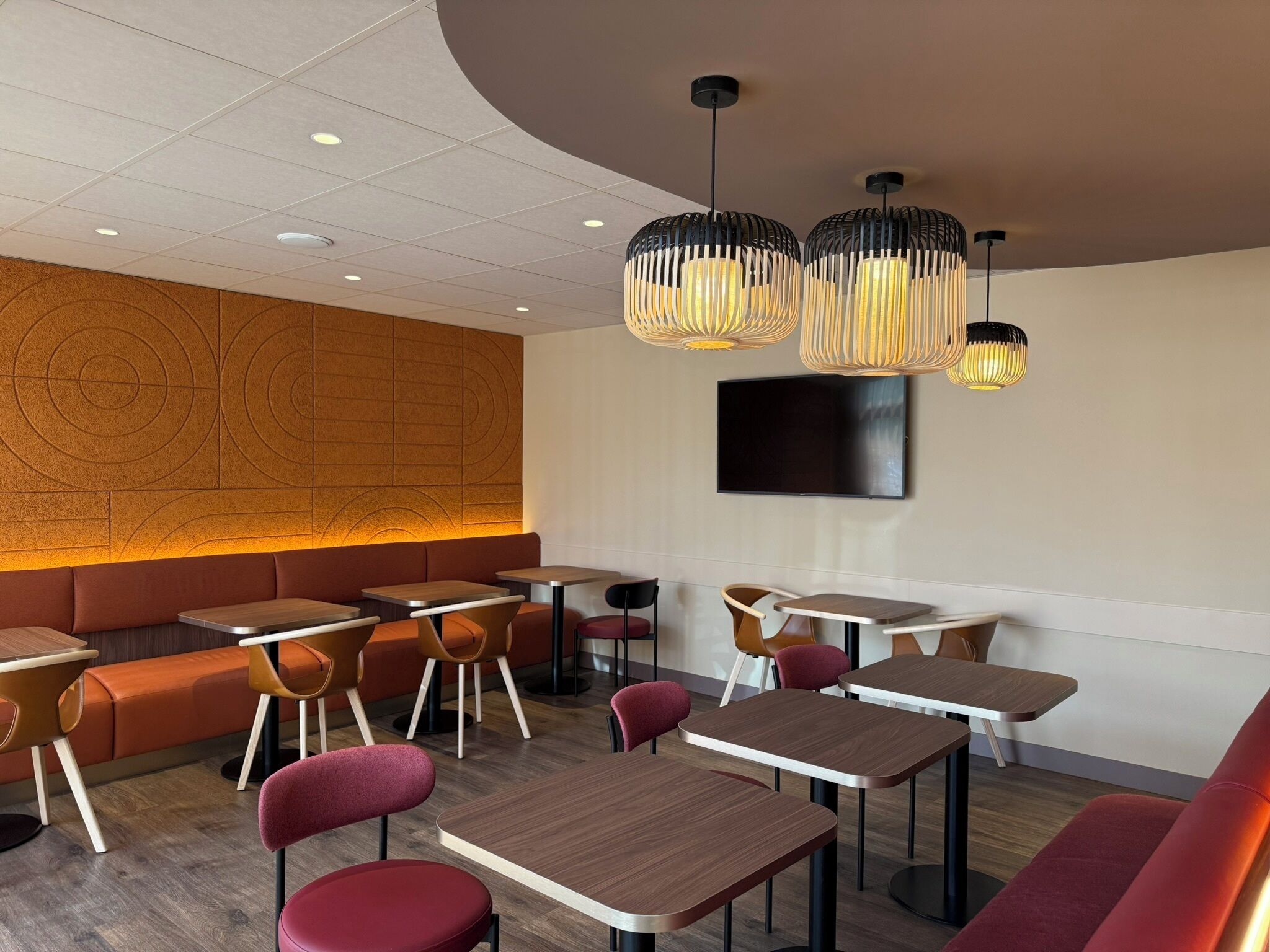 A modern restaurant interior with a curved ceiling, recessed lighting, a flat-screen TV, and a variety of seating options including tables and booths.