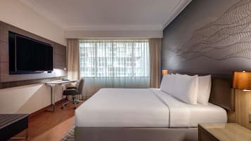 A hotel room with a bed, desk, chair, TV, and a large window with curtains.