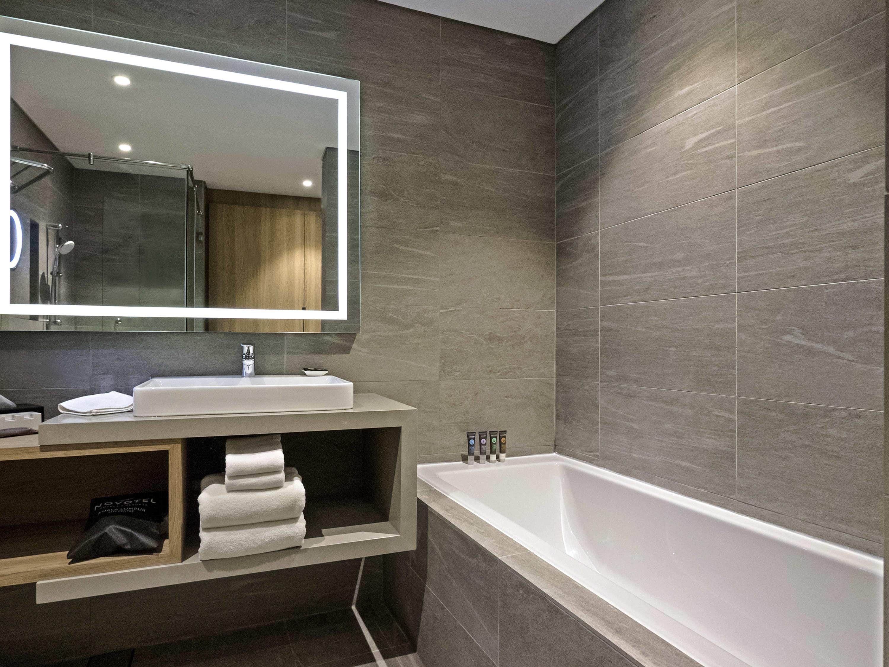 A modern bathroom with a large mirror, a bathtub, and a vanity with a sink and towel rack.