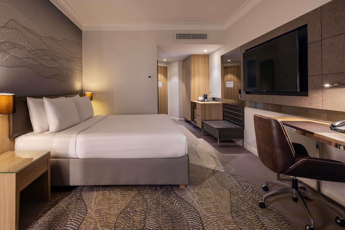 A hotel room with a bed, desk, chair, TV, and a bathroom with a shower and toilet.