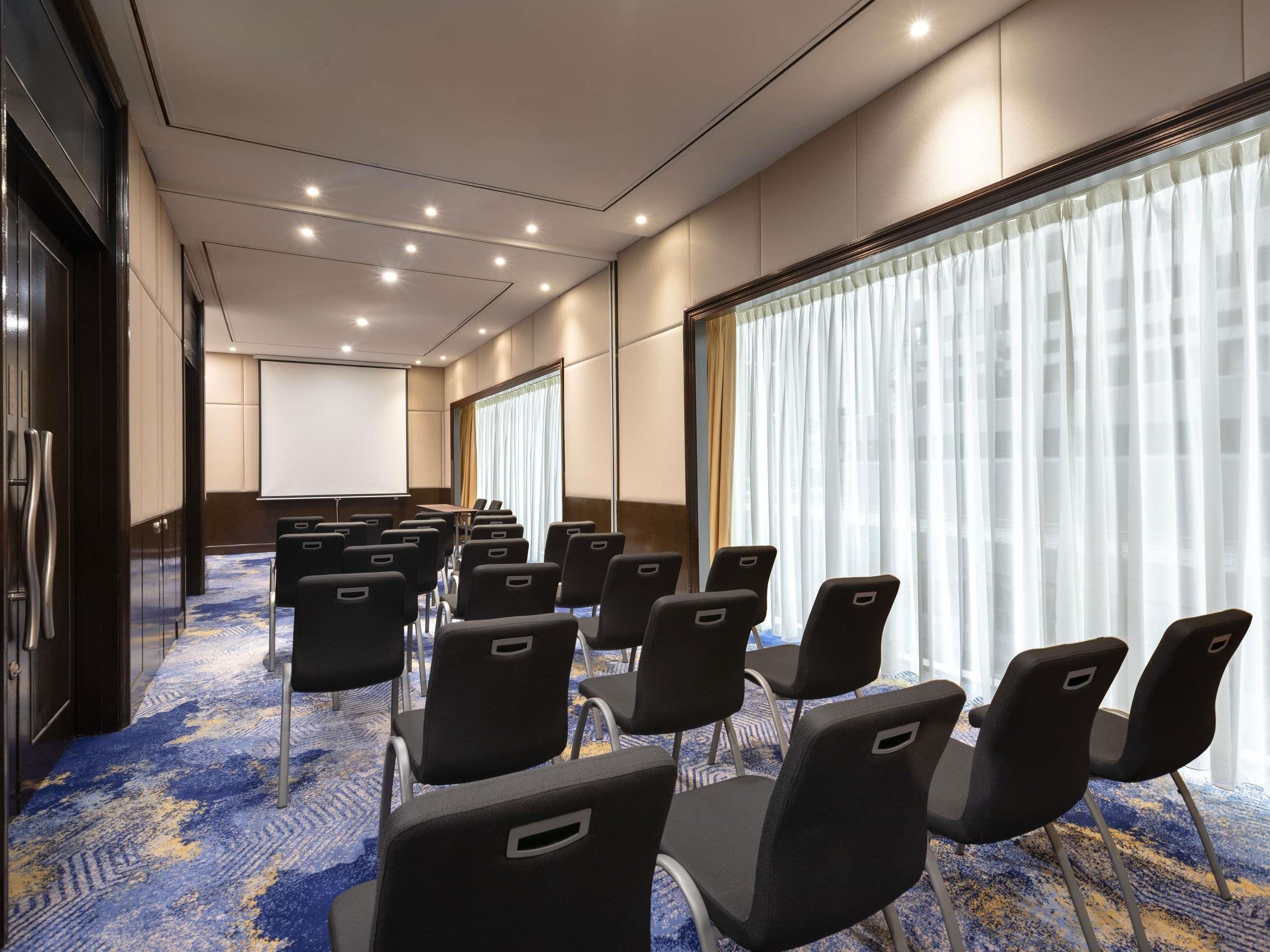 A conference room with rows of chairs, a projector screen, and large windows with curtains.