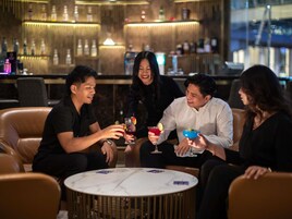 Un grupo de personas sentadas alrededor de una mesa redonda en un área de bar, con una barra de fondo.