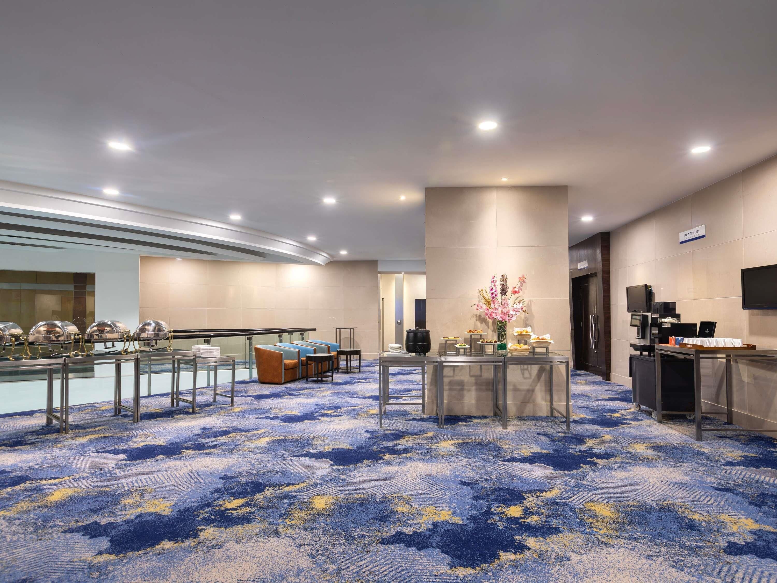 A hotel lobby with a blue patterned carpet, a reception desk, a television, and a sign indicating a 'Platinum' room.
