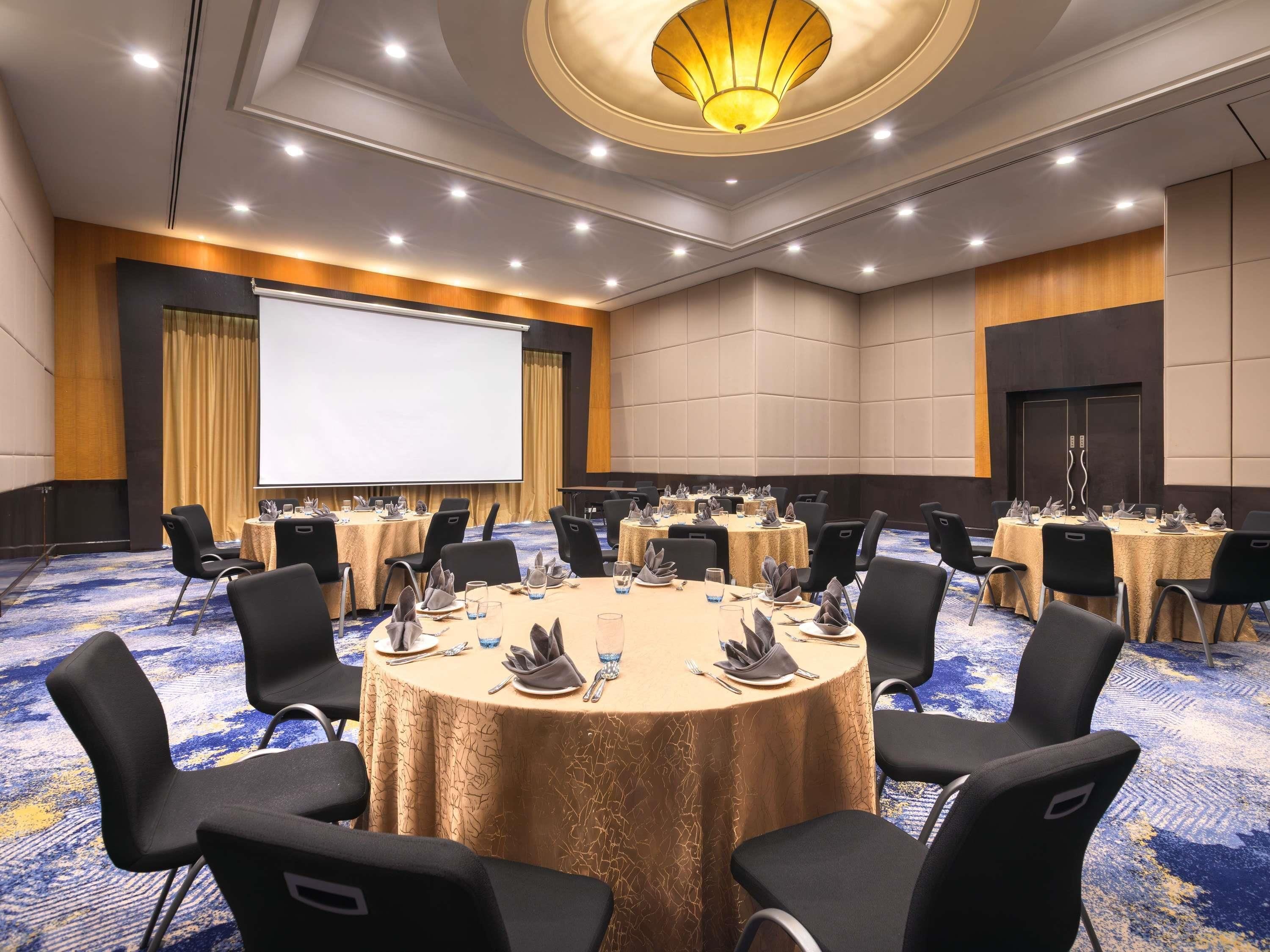 A conference room with round tables, black chairs, and a large screen.