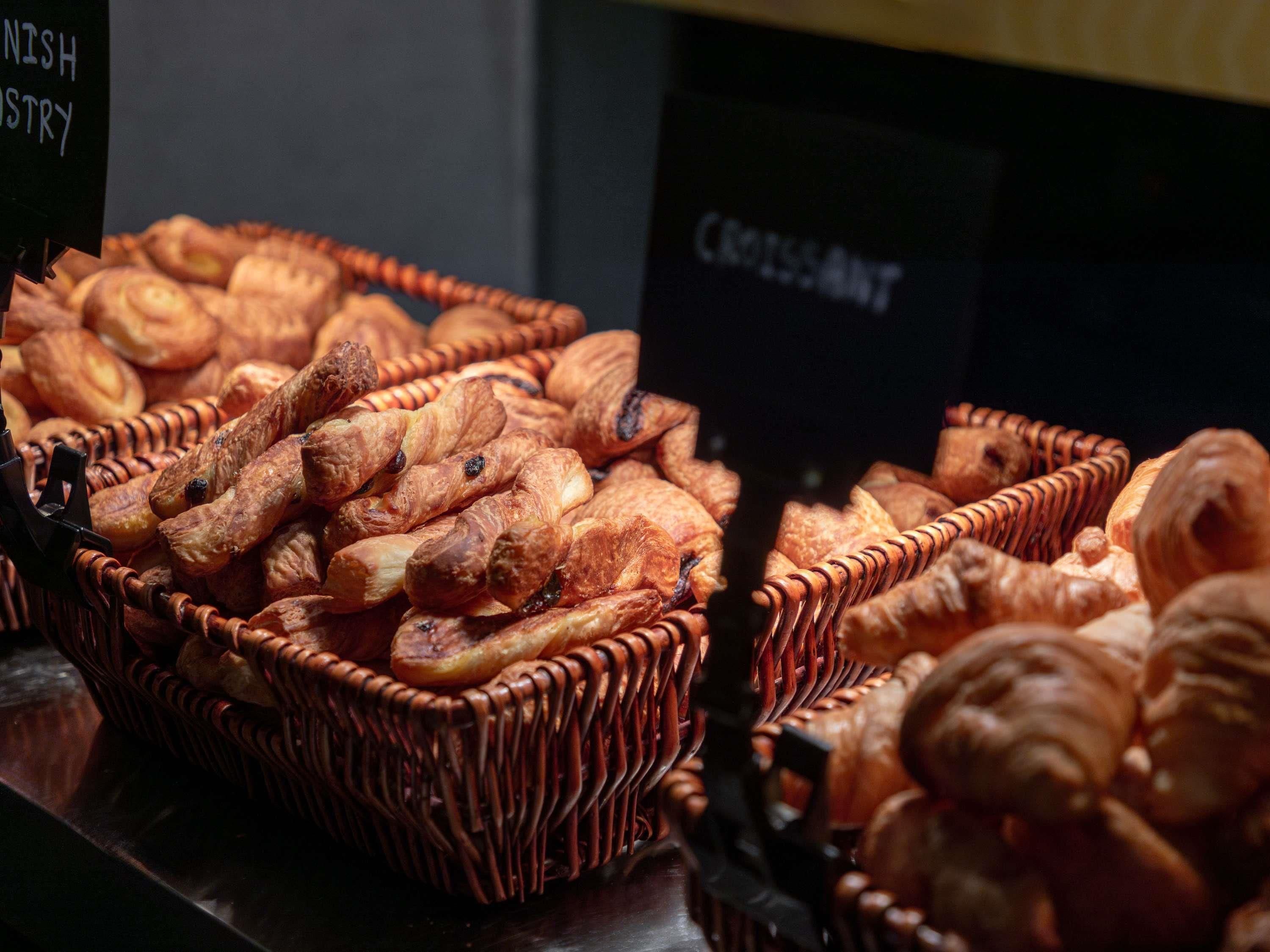 A display of baked goods, including croissants and other pastries, arranged in wicker baskets.
