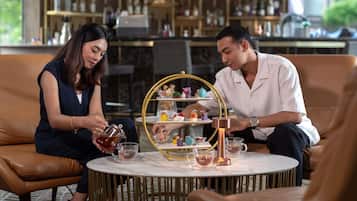 A couple seated at a round table with a tea service, surrounded by leather chairs and a decorative tray.
