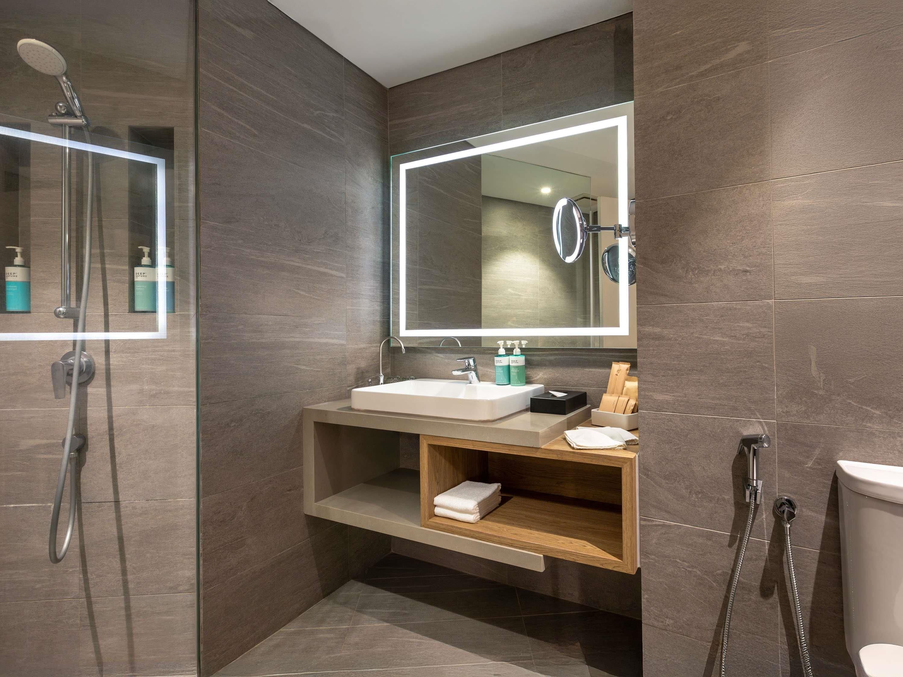 A modern bathroom with a glass-enclosed shower, a large mirror, and a wooden vanity with a sink and storage.