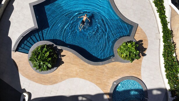 Vista aérea de una piscina de forma singular, rodeada de sillones y sombrillas.
