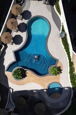 An aerial view of a swimming pool with a unique shape, surrounded by lounge chairs and umbrellas. - Novotel Kuala Lumpur City Centre (Kuala Lumpur)