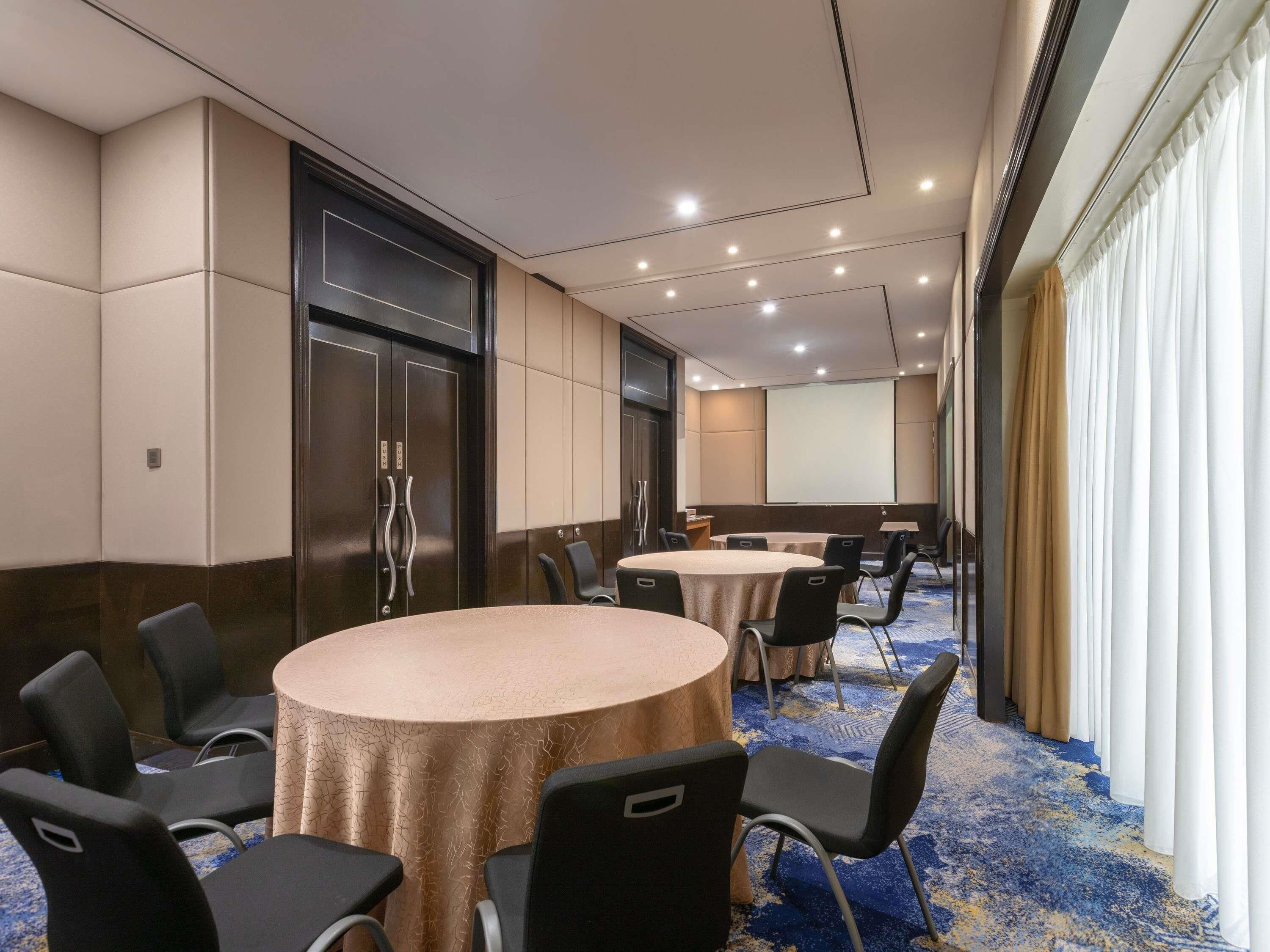 A conference room with round tables, chairs, a projector screen, and a large door.