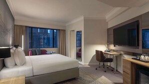 Habitación de hotel con una cama grande, un escritorio con silla, televisión y vistas a la ciudad.