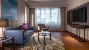 A hotel room with a sofa, armchair, coffee table, TV, and a large window with curtains. - Novotel Kuala Lumpur City Centre (Kuala Lumpur)