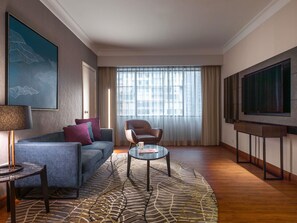 A hotel room with a sofa, armchair, coffee table, TV, and a large window with curtains. - Novotel Kuala Lumpur City Centre (Kuala Lumpur)