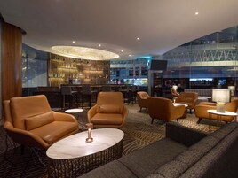 Un'area lounge moderna con divani in pelle, un bar con parete di vetro e un soffitto alto con illuminazione a incasso.