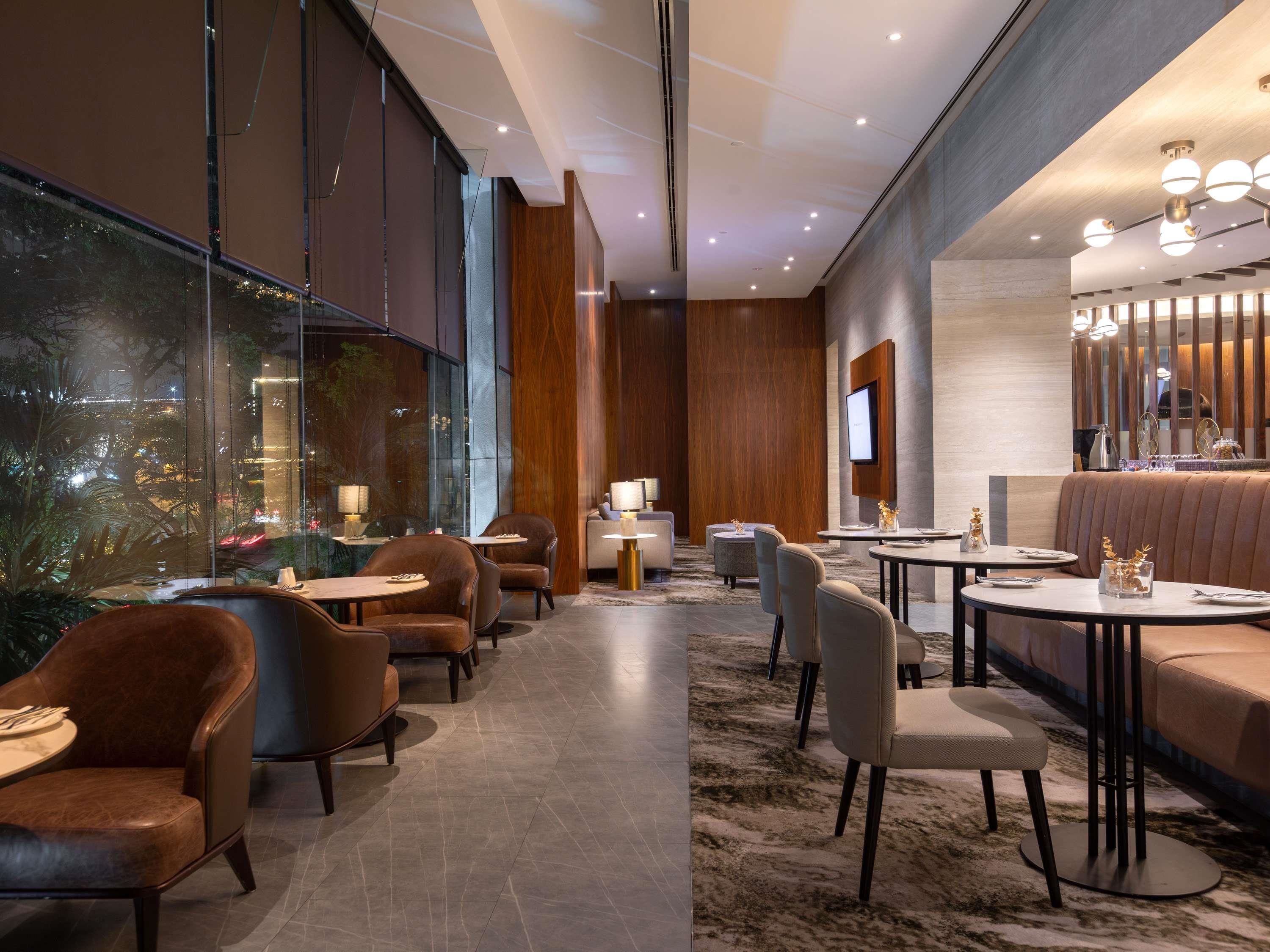 A modern hotel lobby with leather seating, a central bar area, and large windows offering city views.