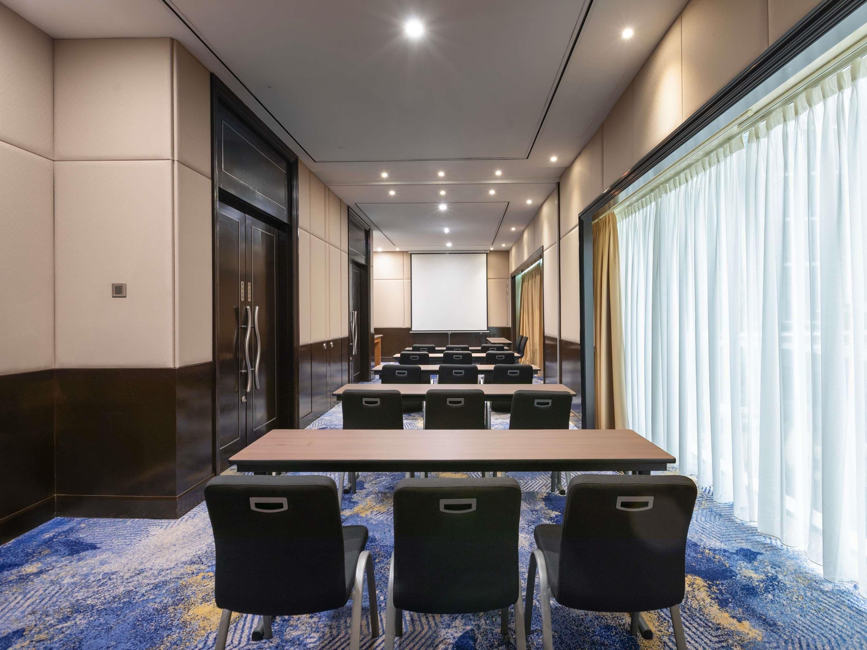 A conference room with tables and chairs, a projector screen, and a large window with curtains.