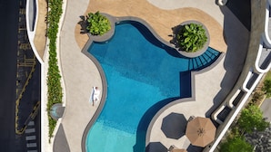 An aerial view of a swimming pool area with a curved design, surrounded by pathways, and shaded by umbrellas. - Novotel Kuala Lumpur City Centre (Kuala Lumpur)