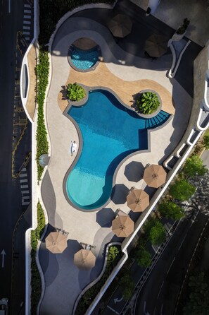 Vista aérea de una zona de piscina con diseño curvo, rodeada de senderos y protegida por sombrillas.