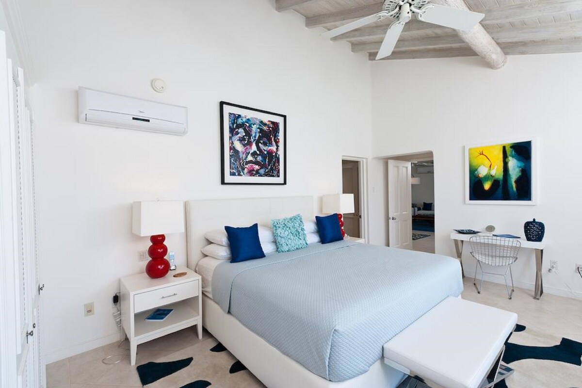 A modern bedroom with a large bed, bedside tables, a desk, and artwork on the walls.