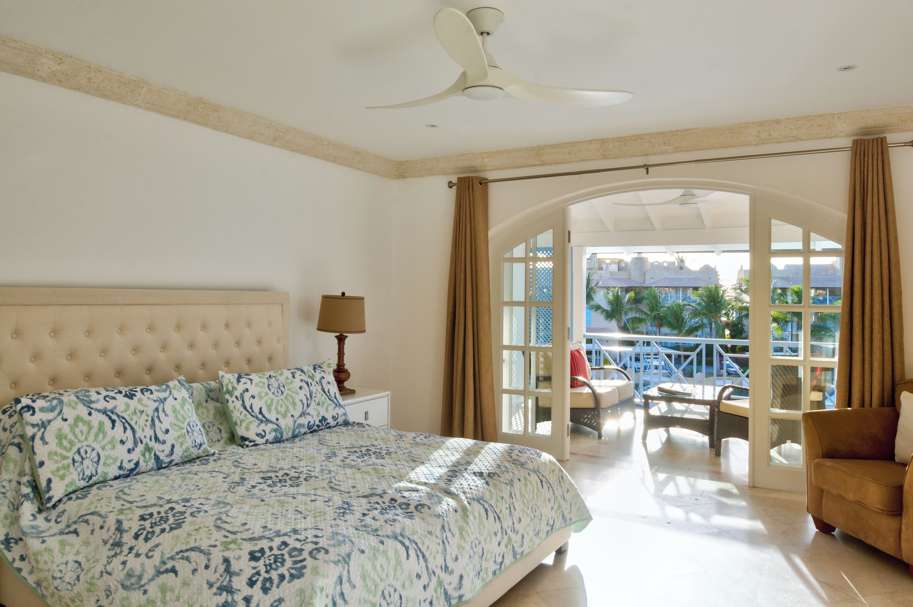 A bedroom with a large bed, a ceiling fan, and a view of a pool and outdoor area.