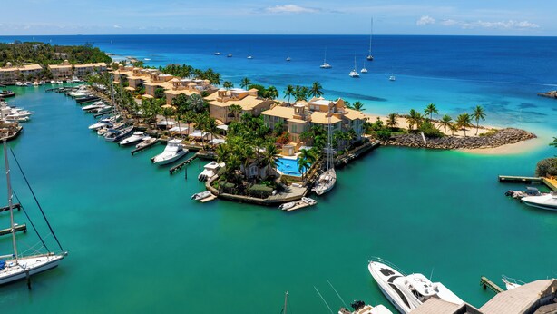 Un puerto deportivo con barcos amarrados, una playa y edificios con piscina.