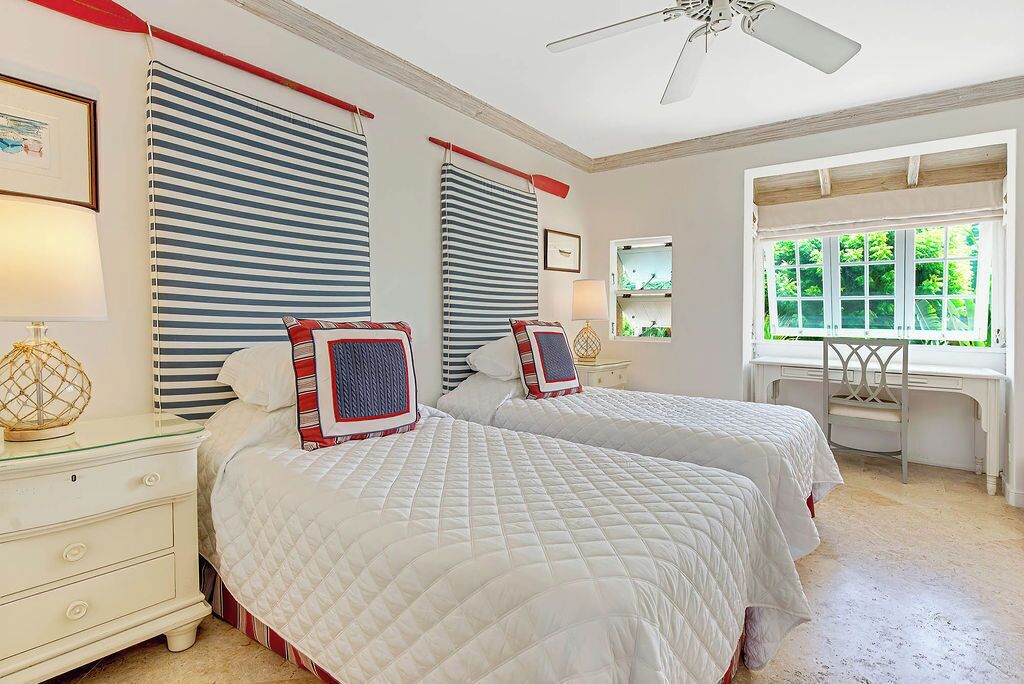 A bedroom with two beds, striped curtains, a desk, and a window with a view of greenery.