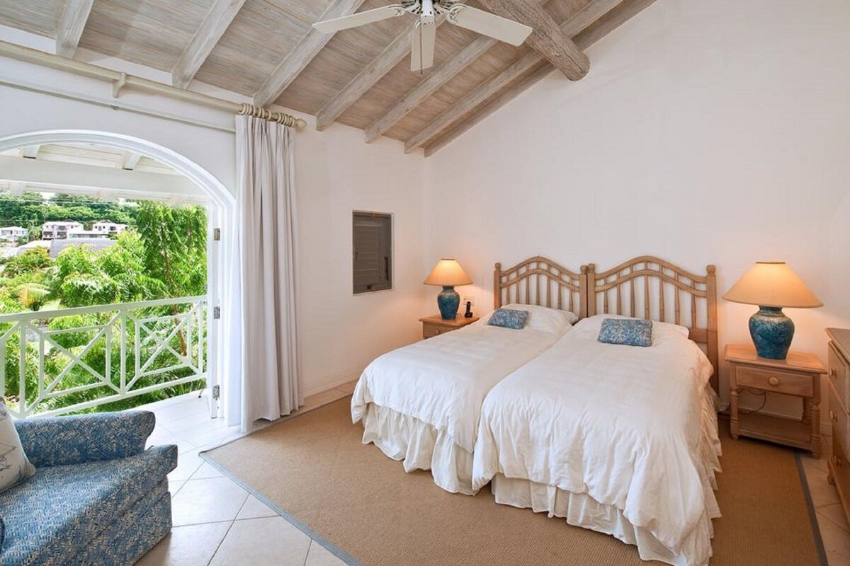 A bedroom with two beds, a balcony with a view, and a ceiling fan.