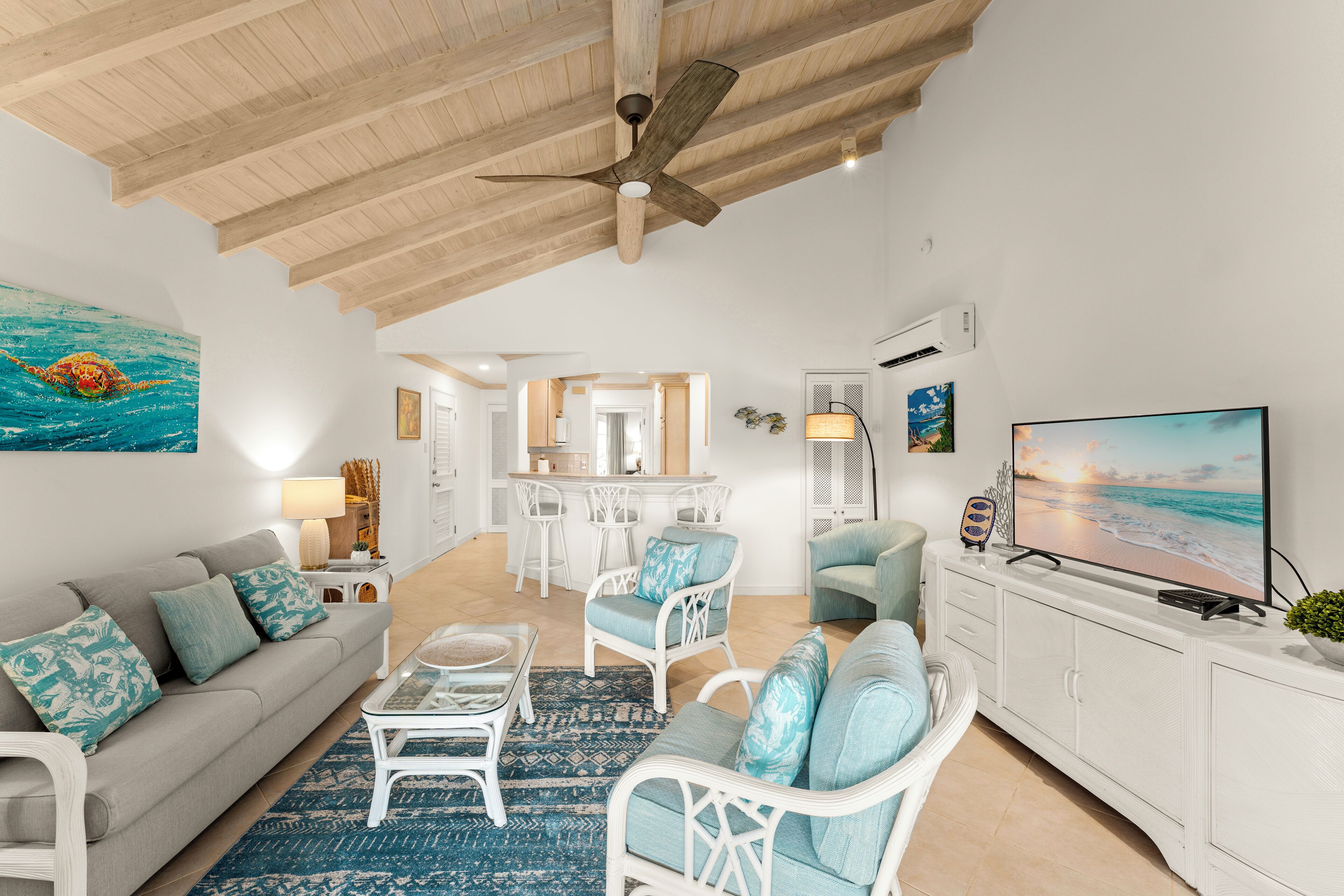 A spacious living room with a ceiling fan, a large TV, and a view of the kitchen and dining area.