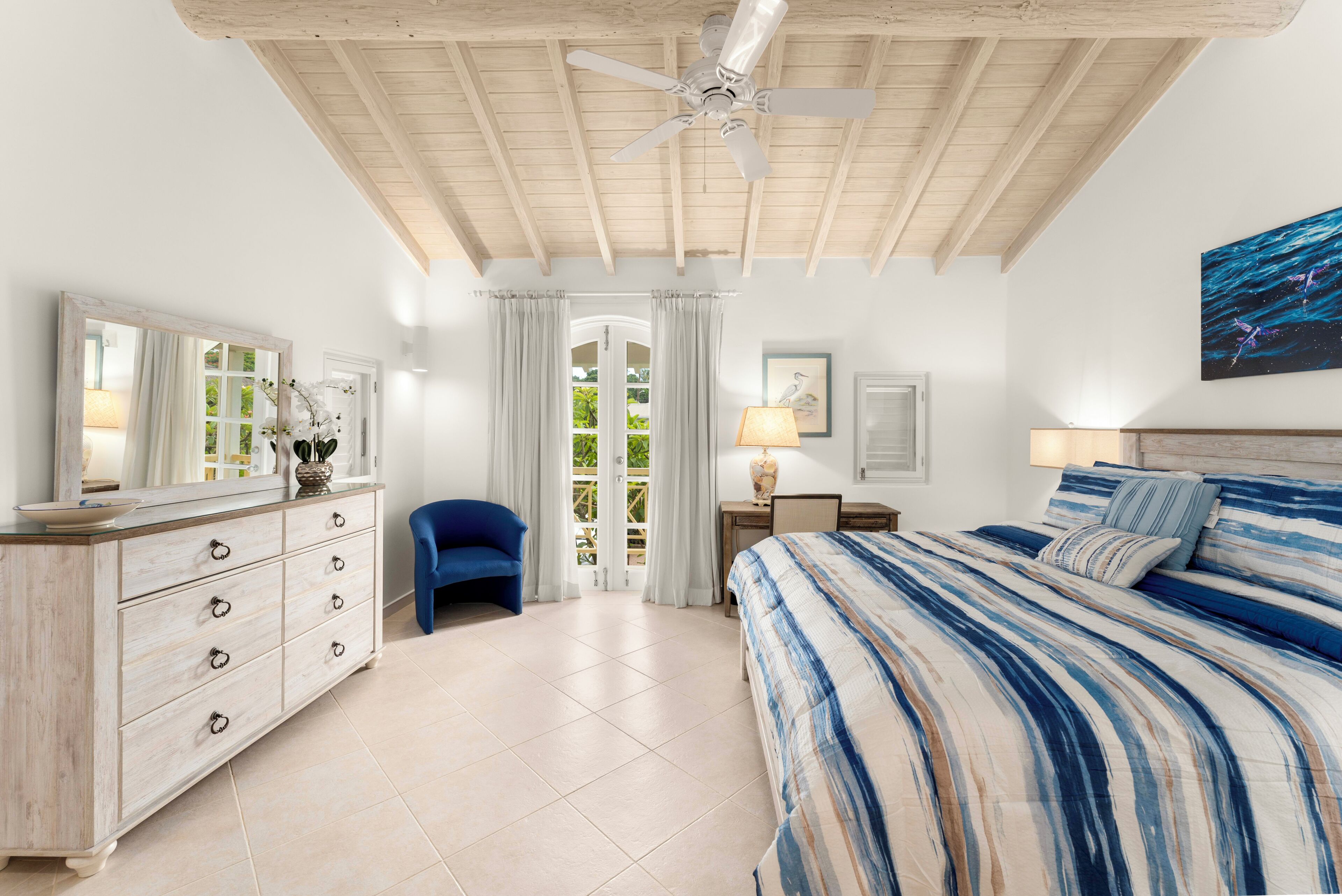 A bedroom with a bed, a dresser, a chair, a ceiling fan, and a window with curtains.