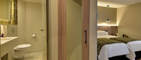 A hotel room with a wooden door, a toilet, a sink, and two beds with white bedding.