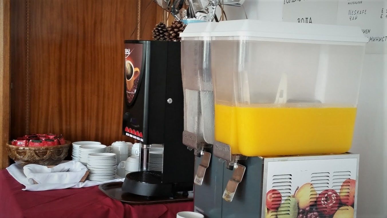 A coffee machine with a transparent water tank, a coffee dispenser, and a stack of white cups and saucers on a table.